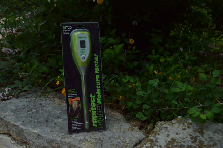 moisture meter in packaging leaning against greenery.